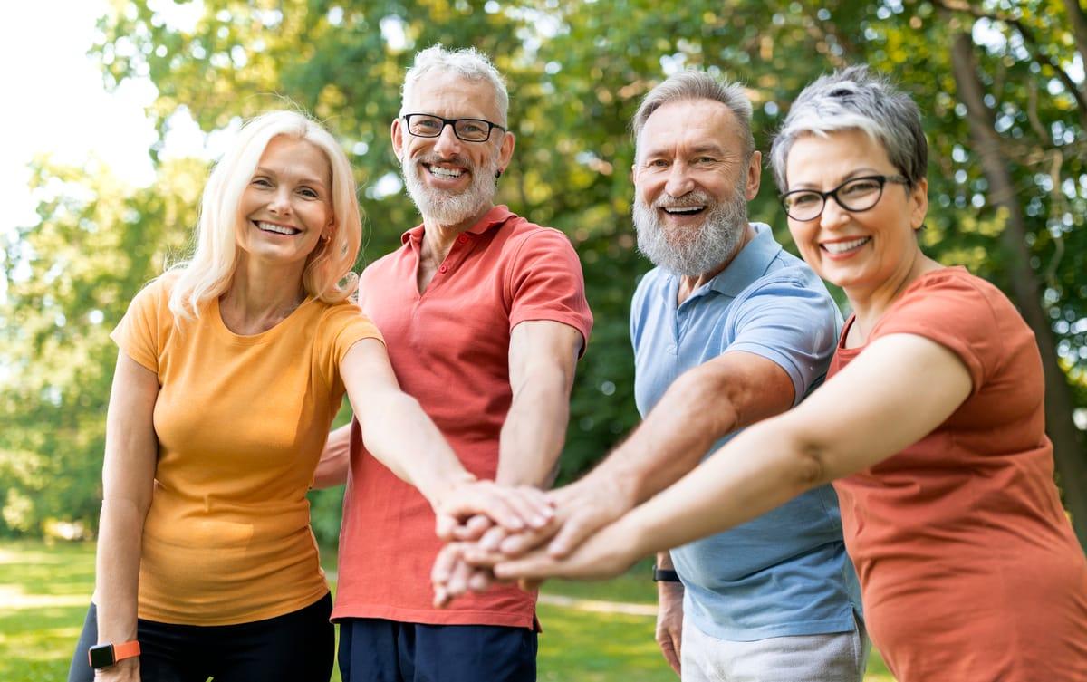 Group of smiling older adults stacking hands after a small group workout