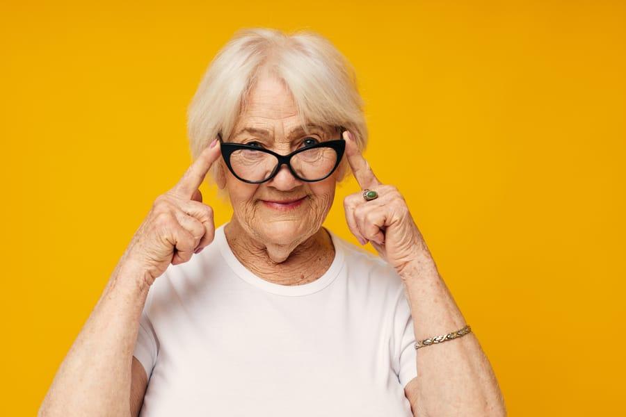 Older woman smiling and pointing to her glasses